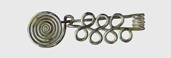 LOT 104 | BRONZE AGE COILED BROOCH | CENTRAL EUROPE, C. 11TH - 10TH CENTURY B.C. copper alloy, in the form of three figure of eight coils, to one end a large coil, to the other a large spring with integral pin resting on a catchplate formed from coil 10.5cm long | £400 - £600